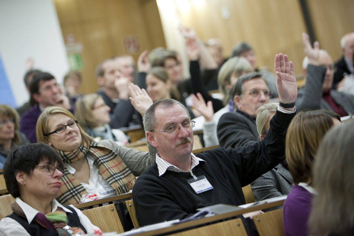 Das Plenum der Veranstaltung gibt durch Handzeichen ein Meinungsbild