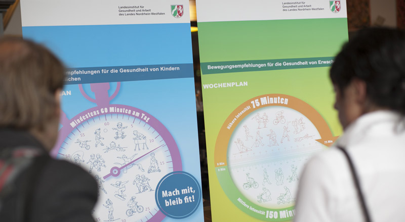 Teilnehmer betrachten die LIGA.NRW-Poster mit Bewegungsempfehlungen für die Gesundheit