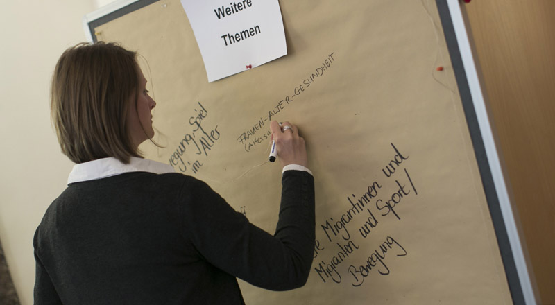 Eine Teilnehmerin schreibt Themenvorschläge auf eine Pinnwand